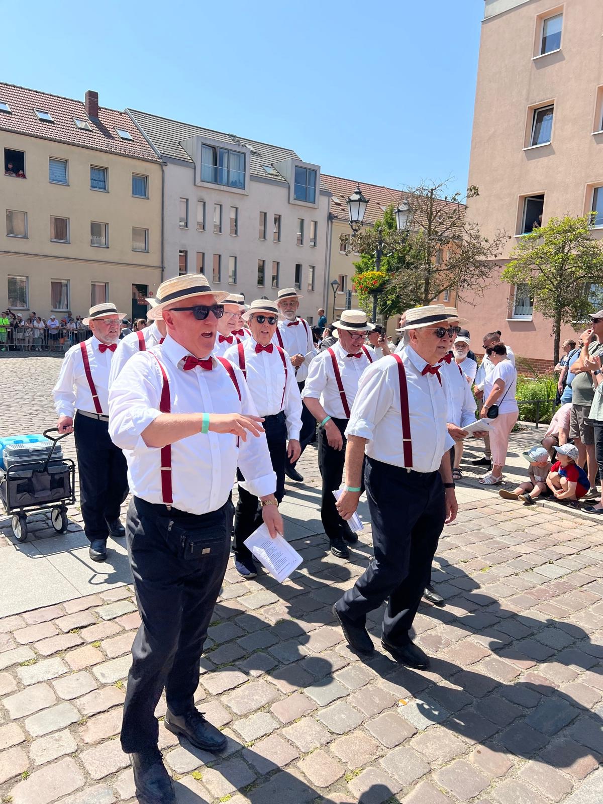 Sänger von Teutonia Ladeburg singen bei einem Umzug mit Strohhüten und roten Hosenträgern